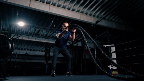 joven culturista masculino haciendo ejercicios con cuerda en las manos en el gimnasio preparando la motivación de la competencia culturismo - Metraje, vídeo