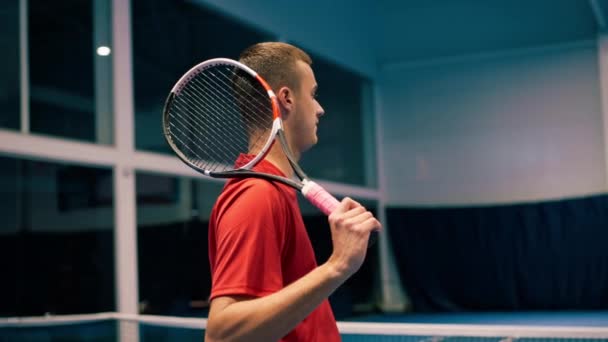 молодий чоловік на критому тенісному корті, який бив м'яч з ракеткою в стрибку, служить під час гри тенісного інструктора професійний спорт - Кадри, відео