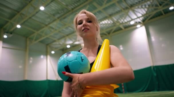 retrato de una joven sonriente a la que le encanta el fútbol de pie en el campo sosteniendo equipo deportivo en sus manos después del entrenamiento - Metraje, vídeo