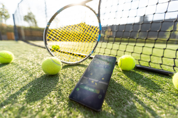 マルーンバックグラウンド上のテニスラケットのボールによるスポーツシューズとデジタルタブレットの高角度ビュー. 高品質の写真 - 写真・画像
