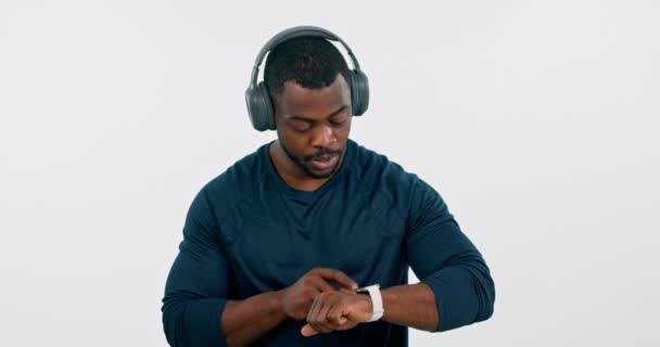 Άσκηση, μουσική και έξυπνο ρολόι με έναν μαύρο αθλητή στο στούντιο σε λευκό φόντο για να παρακολουθείτε την υγεία του. Άσκηση, εκπαίδευση και εφαρμογή προπόνησης με ένα νεαρό αθλητή που ελέγχει την ώρα με ακουστικά. - Πλάνα, βίντεο