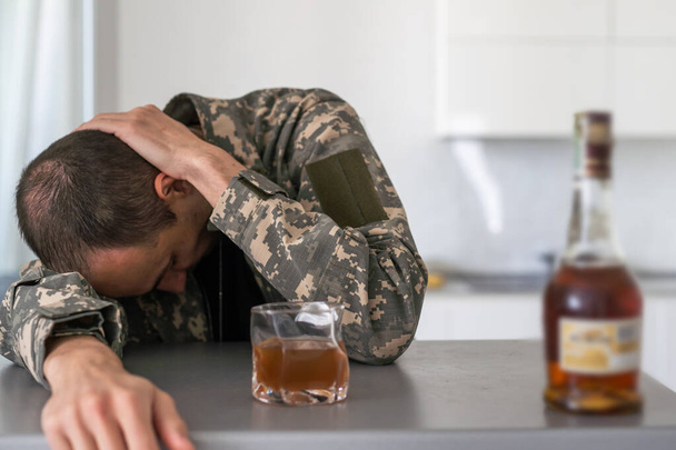 Ein Mann sitzt zu Hause mit einer Flasche Schnaps und trinkt Whiskey, trinkt alkoholischen Alkoholmissbrauch, Sucht und Depressionen. Hochwertiges Foto - Foto, Bild
