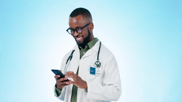 ドクター, 男とオンラインコンタクトのためのスタジオで携帯電話で幸せ, ブルーバックグラウンドで医療通知やテレヘルス情報を読んで. アフリカの外科医, 笑うか,デジタルアプリを検索するためにスマートフォンにタイピング. - 映像、動画