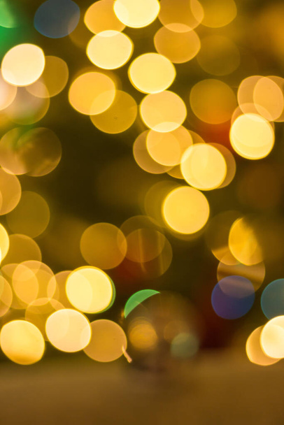 Golden Christmas lights on dark background, unfocused. Illuminated bokeh background. Glowing lights, defocused. Winter holidays magic. Golden stardust lights. Christmas decoration. Festive illumination.  - Photo, Image