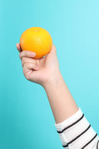 Azjatka trzymająca pomarańczę w dłoni na zielonym tle. - Zdjęcie, obraz