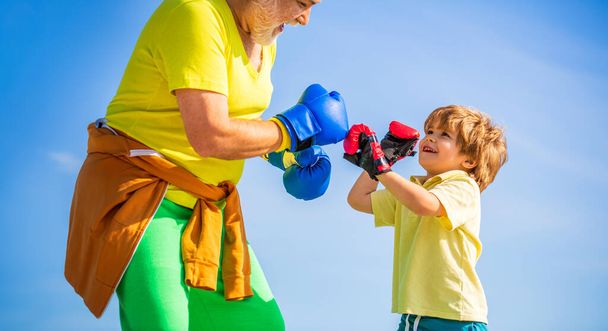 Little boy sportsman at boxing training with coach. Sports man coaching boxing little boy in red boxing gloves. Little boy doing boxings exercise with grandfather. Father is training his son boxing. - Foto, Imagem