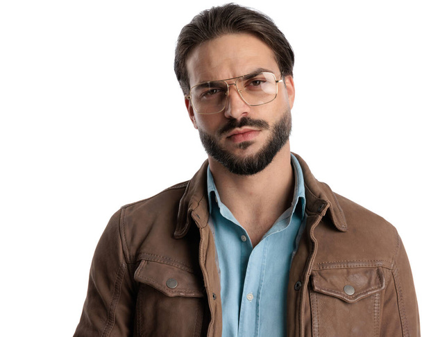 guapo hombre fresco con gafas en chaqueta marrón mirando hacia adelante en frente de fondo blanco  - Foto, imagen