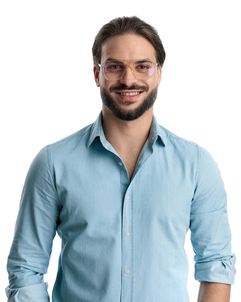 happy casual guy in denim shirt with glasses looking forward and smiling in front of white background - Фото, изображение