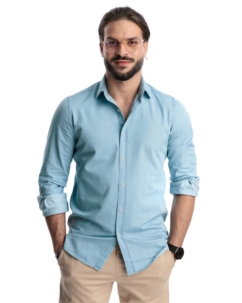 ポケットに手を握る青いジーンズのシャツを身に着けている魅力的なカジュアルな男性は,白い背景で前方と笑顔を見ています  - 写真・画像