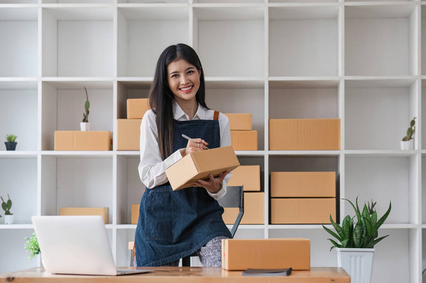 Portrait business woman smile and use laptop checking information on parcel shipping box before send to customer. Entrepreneur small business working at home. SME business online marketing.. - Photo, Image