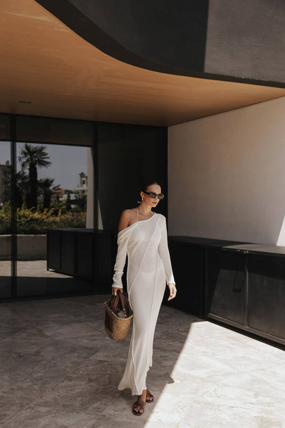 moda foto ao ar livre de mulher bonita com cabelo escuro em vestido branco elegante e acessórios posando perto da janela do espelho do hotel - Foto, Imagem