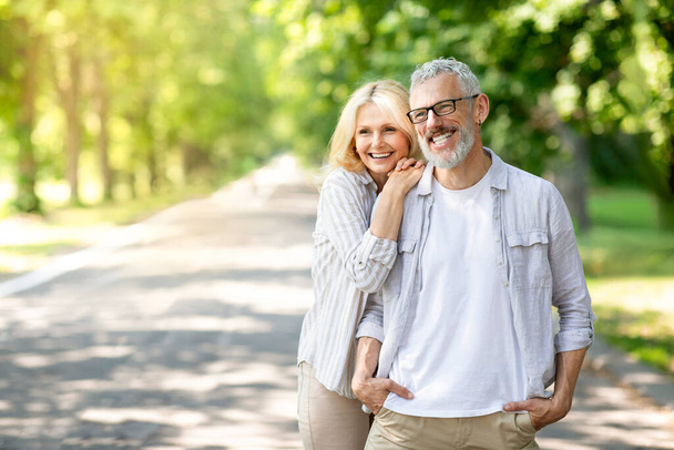 Szczęśliwej emerytury. Romantyczna para seniorów relaksująca się razem w Sunny Park, wesoły dojrzały mężczyzna i kobieta Obejmujący i patrzący w dal, uśmiechnięci starsi małżonkowie cieszący się spędzaniem czasu na świeżym powietrzu, przestrzeń do kopiowania - Zdjęcie, obraz