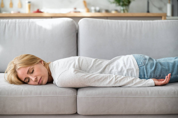 Donna esausta sdraiata sul divano comfort a casa, facendo un pisolino di giorno, sensazione di mancanza di energia dopo una notte insonne o di lavoro eccessivo. Le donne stanche non hanno alcuna motivazione per lavorare. Concetto di affaticamento - Foto, immagini
