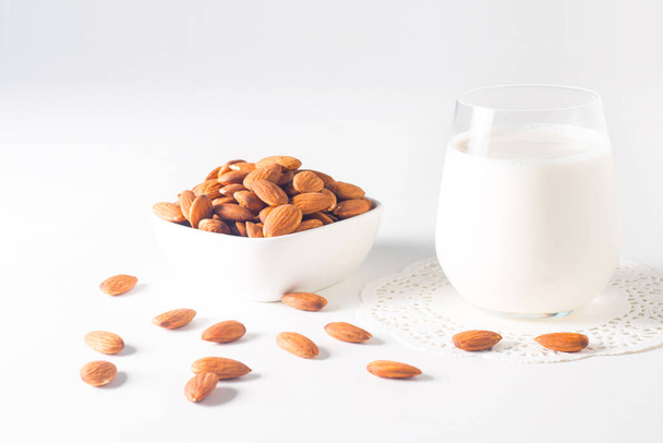 Βιολογικό γάλα αμυγδάλου σε ποτήρι με ωμά αμύγδαλα σε λευκό τραπέζι  - Φωτογραφία, εικόνα