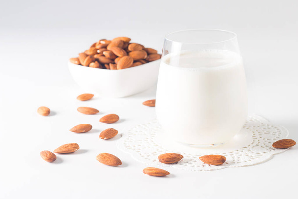 Bardakta organik badem sütü ve beyaz masada çiğ badem.  - Fotoğraf, Görsel