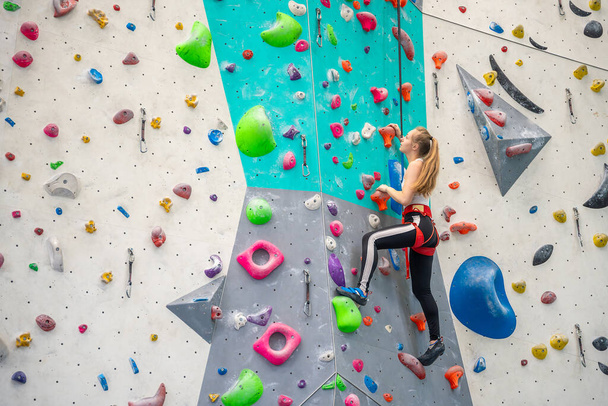 Escalade jeune femme accrochée à des crochets colorés sur le mur artificiel d'escalade à l'intérieur du centre sportif de Prague. Sports extrêmes et concept de bloc. Photo de haute qualité - Photo, image
