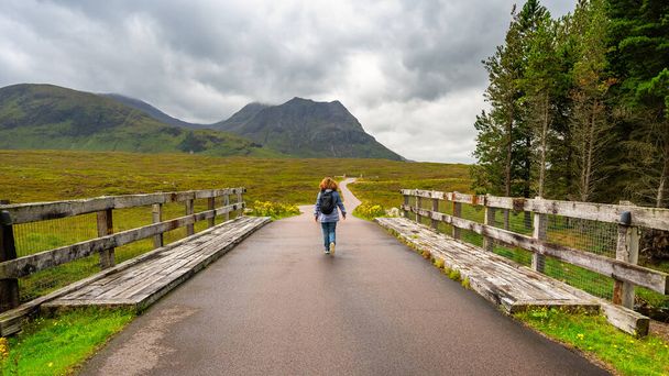 Žena turistka procházka přes most přes řeku ve vysokohorském prostředí, Glencoe, Skotsko - Fotografie, Obrázek