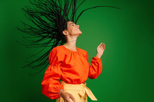 Ελκυστική νεαρή γυναίκα με dreadlocs χορό και αναζητούν χαρούμενη σε πράσινο φόντο - Φωτογραφία, εικόνα