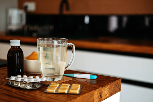 Natural and medical cold and flu remedies on table at home. Cold and flu influenza fall autumn and winter season. Cup with hot tea, lemon, thermometer pills and capsules. - Photo, Image