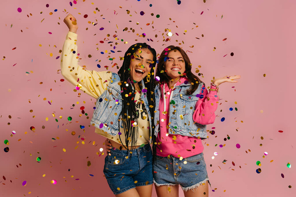 Two joyful young women in colorful wear dancing against red background - Photo, Image