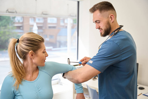 High-qualified doctor checking triceps and biceps reflex of young woman client of the neurological department, health check-up, rehabilitation after injury - Foto, imagen