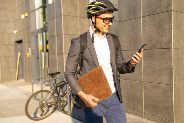 Przystojny młody biznesmen w garniturze z rowerem przy użyciu smartfona na ulicy miasta. - Zdjęcie, obraz