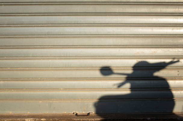 Fondo de una vieja puerta de garaje de metal cerrado. El sol de la tarde proyecta la sombra de un scooter en la puerta del garaje. Hay espacio para el texto. - Foto, Imagen