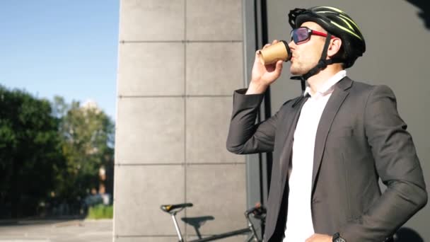 Knappe jonge volwassen man draagt pak in veiligheidshelm met een koffie voor het rijden op zijn klassieke fiets naar het werk in de ochtend. - Video