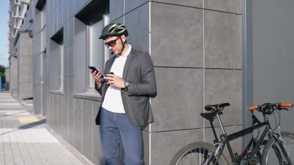 Knappe jonge volwassen man draagt pak in veiligheidshelm met een koffie voor het rijden op zijn klassieke fiets naar het werk in de ochtend. - Video