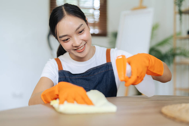 Mladá žena čištění pomocí spreje a otírání stolu s mikrovláknitou látkou v obývacím pokoji. - Fotografie, Obrázek