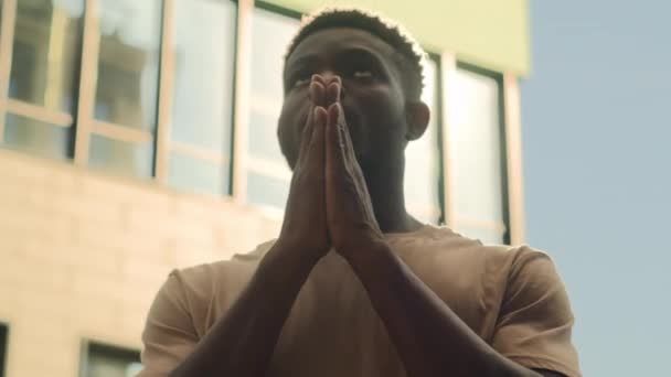 Afro-Amerikaanse man etnische man man in de stad buiten in zonlicht zonnige achtergrond zonnestralen zonlicht gevouwen palmen handen in gebed geloof vragen god hoop religie aanbidding geloof bidden geloven bidden - Video