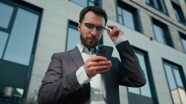 Gondolatos üzletember felnőtt kétes kaukázusi férfi szabadban használja mobiltelefon férfi munkáltató üzletfejlesztő vezérigazgató vállalkozó dolgozik a városban okostelefon digitális app e-commerce chat online - Felvétel, videó