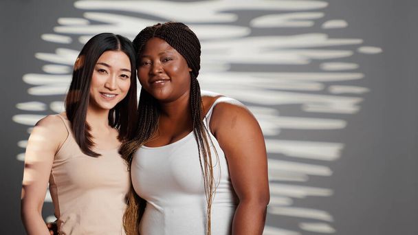 Happy diverse ladies hugging and posing in studio, promoting wellness and bodycare, self acceptance. Flawless young women with different body shapes and skintones showing self love. - Photo, Image