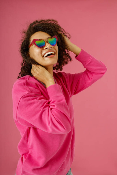 Donna sorridente in maglione sta toccando i capelli e guardando lato in piedi su sfondo rosa studio - Foto, immagini