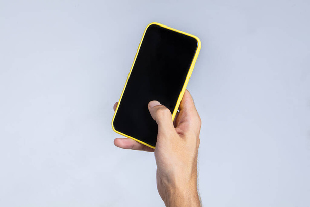 Main d'un homme tenant un smartphone avec sa main droite et opérant sur l'écran avec son pouce. L'écran du téléphone est blanc et noir, adapté pour placer des publicités ou des images. Fond blanc - Photo, image