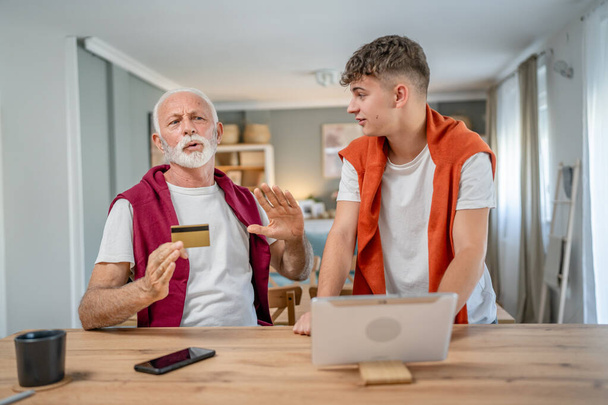 Ein Teenager junger Mann und ältere kaukasische männliche Großvater sitzen zu Hause mit Kreditkarte und Laptop-Computer einkaufen Online-Nutzung des Internets für Online-Einkauf aktive moderne Senior - Foto, Bild