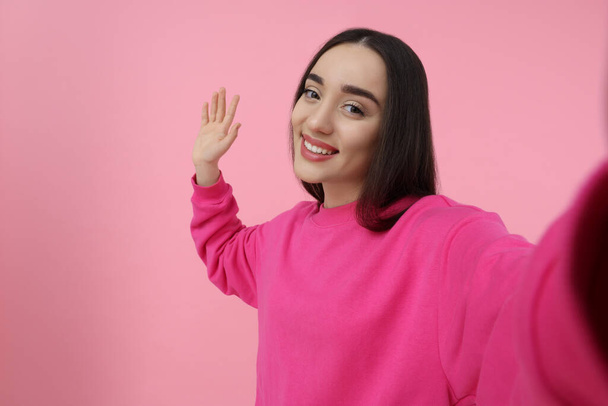 Smiling young woman taking selfie on pink background, space for text - Foto, imagen