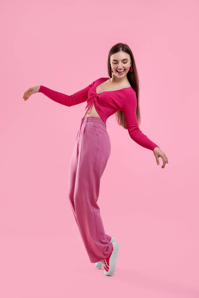 Beautiful young woman in pink clothes dancing on color background - Фото, зображення