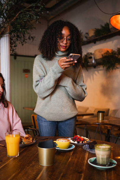 Mujer joven tomando una foto con su teléfono inteligente del almuerzo que está teniendo con sus amigos - Foto, imagen