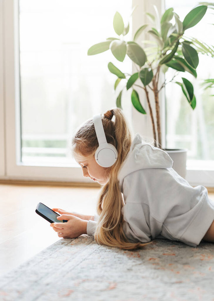 Hymyilevä pikkutyttö kuuntelemassa musiikkia lattialla
 - Valokuva, kuva