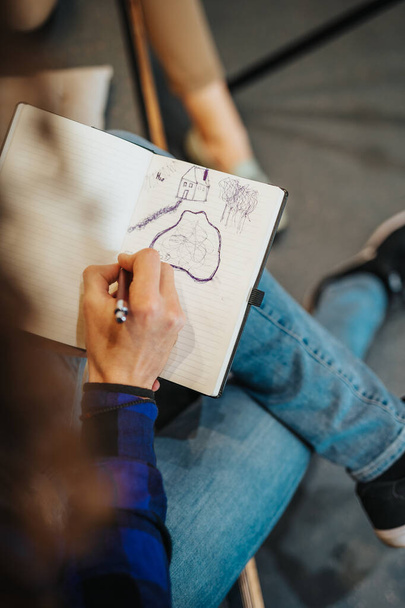 Detailní záběr muže držícího pero a kreslícího domy a jezera ve svém zápisníku v kanceláři - Fotografie, Obrázek