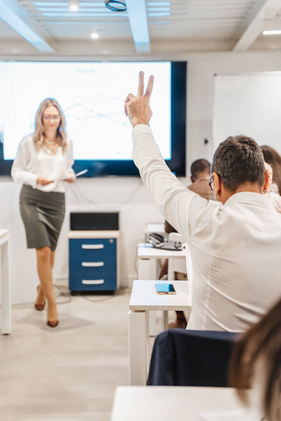 ブロンド,女性,ビジネストレーナーが何かを説明しながら質問するために手を挙げるシニアビジネスマン - 写真・画像