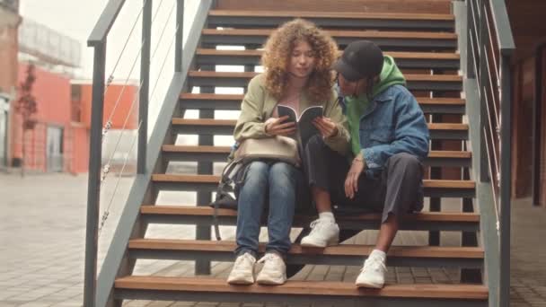 Full length slowmo o multiraciale eerstejaars student paar samen studeren op trappen buiten de campus - Video