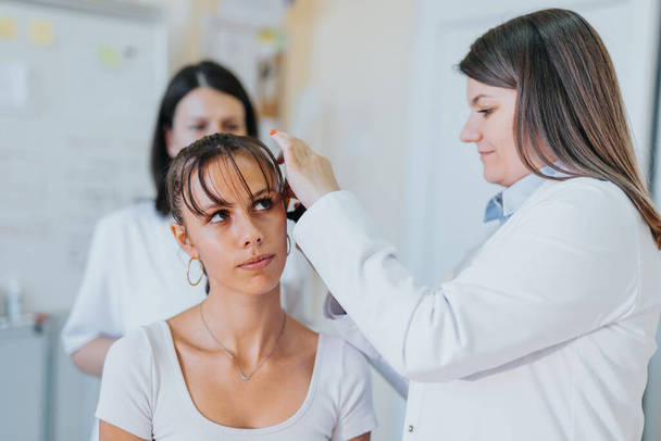 Μια έμπειρη γυναίκα γιατρός εξετάζει την όραση, την ακοή και το λαιμό ενός νεαρού ασθενούς σε μια κλινική. - Φωτογραφία, εικόνα