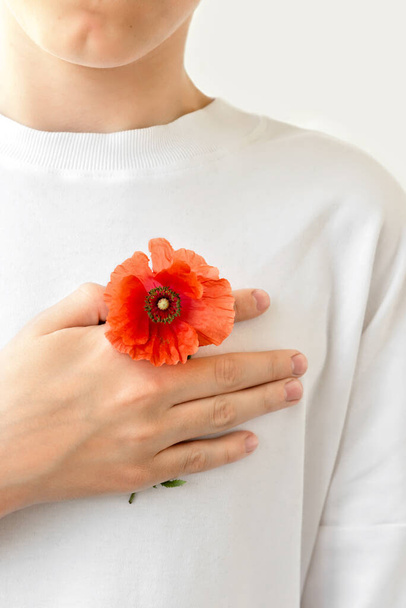 Teenage boy in white t-shirt holding hand with red poppy on chest near heart. Symbol of Remembrance day, Armistice day, Memorial day. Lest we foget concept. - Photo, Image