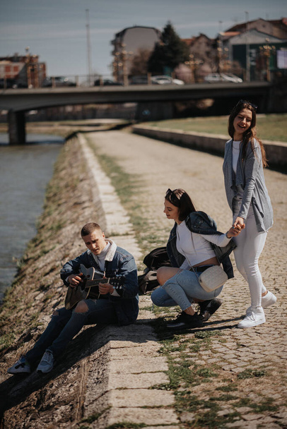 Tre migliori amici che suonano la chitarra e cantano vicino al fiume in città - Foto, immagini
