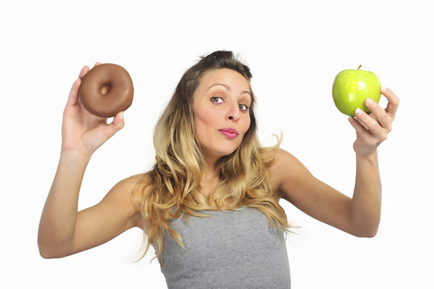 Attractive woman holding apple and chocolate donut in healthy fruit versus sweet junk food temptation - Photo, Image