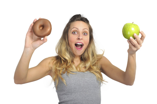 Mulher atraente segurando maçã e donut de chocolate em frutas saudáveis versus doce junk food tentação
 - Foto, Imagem