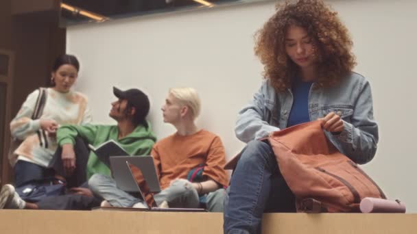 Mittlere Verlangsamung einer jungen kaukasischen Studentin, die ihr Copybook aus der Tasche holt und Laptop benutzt, während sie sich auf den Unterricht am College vorbereitet - Filmmaterial, Video