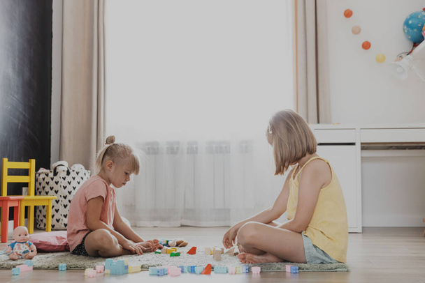 Dzieci bawią się kolorowymi plastikowymi klockami. Dzieci siedzące na piętrze w domowej sypialni, przedszkolu, pokoju dziecinnym. Edukacja ekologiczna gra dla dzieci. słodkie małe siostry mając zabawy razem - Zdjęcie, obraz